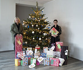 Zwei Frauen mit Geschenken vor einem Weihnachtsbaum | Mitarbeitende der Fondsdepot Bank erfüllen Wünsche von Kindern des Jugendhilfehauses St. Elisabeth in Hof